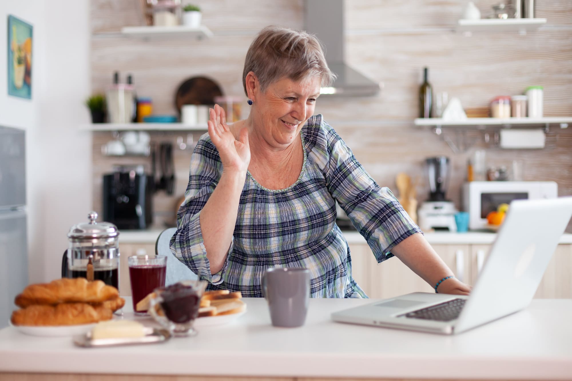 A woman waves at the camera on her laptop