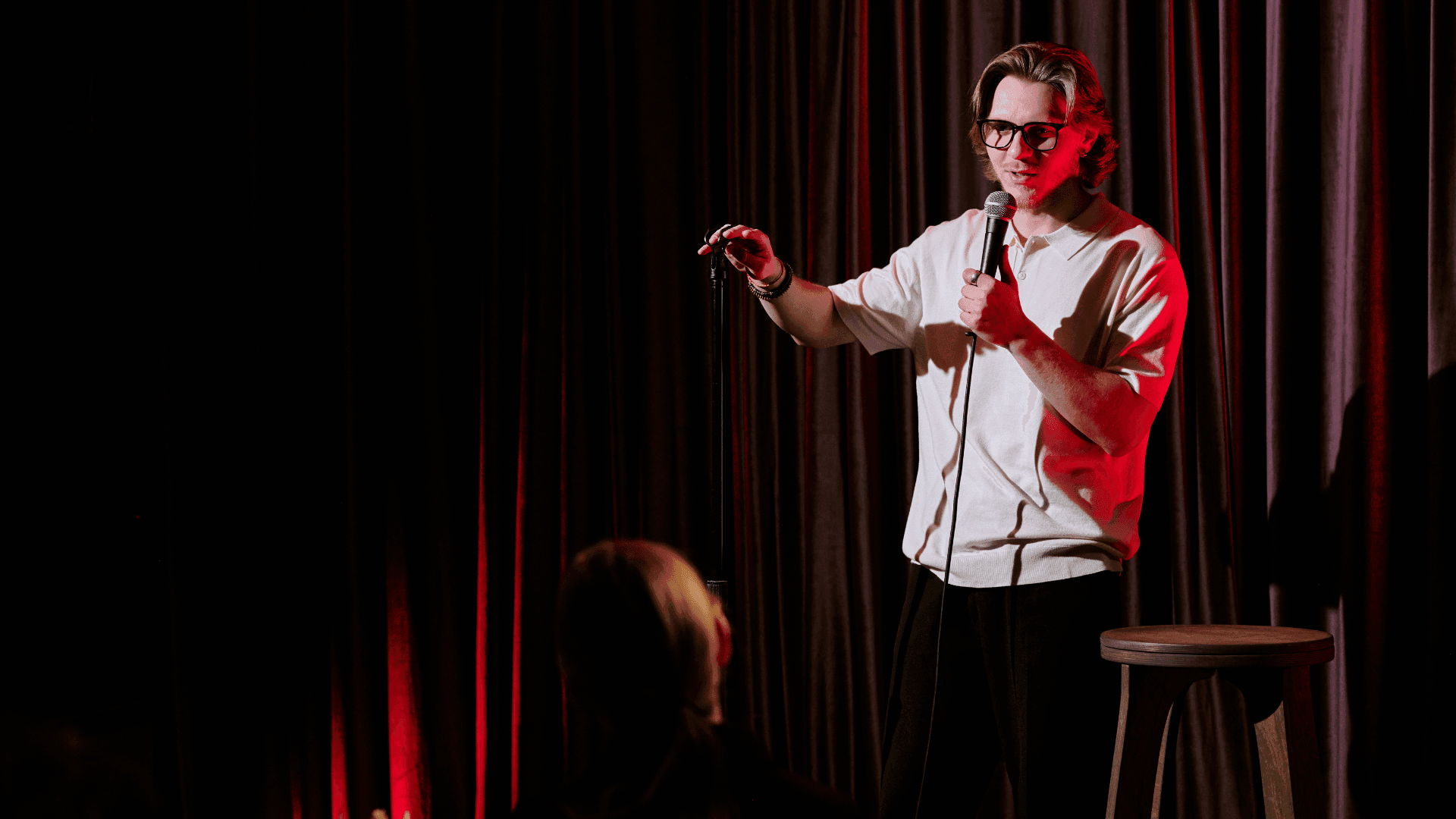 Man holding a mic at a comedy show with a curtain in the backgroun